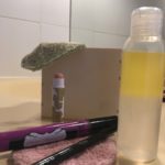 Un flacon de démaquillant entouré de cotons colorés et de produits de maquillage (mascara, crayon, baume à lèvres)